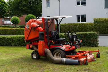Büyük bir çim toplama sistemiyle donatılmış kırmızı bir çim biçme makinesi. Konut alanındaki iyi korunmuş bir çimenliğe park edilmiş..