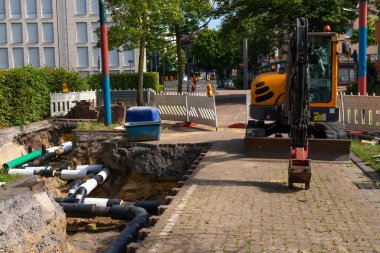 Kentsel boru hatlarının kurulumu ve bakımı. Kurulum için hazırlanmış büyük borular, hendek ve kazıcılı inşaat alanı.