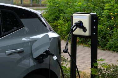 Bir elektrikli araba halka açık bir şarj istasyonuna bağlanıyor, yeşil, kentsel bir ortamda elektrikli araçların büyüyen altyapısını vurguluyor...