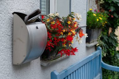 Pencere kenarındaki bir kutunun içinde gazete ve canlı çiçeklerle dolu metal bir posta kutusu konut binasında hoş geldin manzarası yaratıyor..