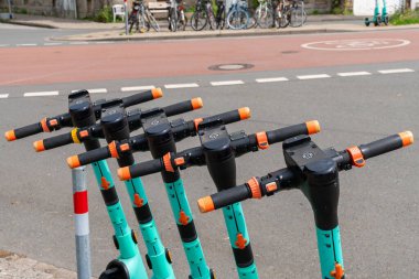 Beş elektrikli scooter düzgün bir şekilde kaldırımda park edilmiş, güneşli bir günde kullanıma hazır..