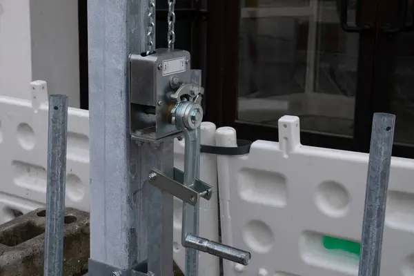 Stock image Close-up of a manual winch mechanism used for lifting and adjusting construction materials. The background includes a white barrier and building entrance.