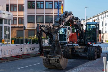 İki büyük kazıcı, beyaz güvenlik bariyerleri ve modern bir binanın bitişiğindeki bir inşaat sahasına park etmiş..