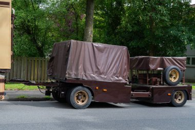 Kahverengi teslimat karavanı caddeye park edilmiş ve kargoyu kaplayan muşambalarla dolu.