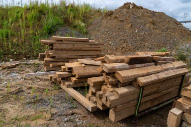 Bir yığın ahşap kiriş, seyrek bitki örtüsüyle çevrili bir çakıl yığınının yanında duruyor..