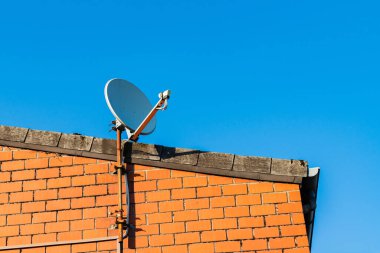 Tuğla bir evin çatısındaki uydu anteni parlak mavi bir gökyüzüne karşı.
