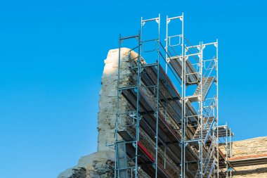 Büyük bir yapı, antik taş kalıntıları üzerinde devam eden restorasyon çalışmalarını destekliyor. İşçiler kritik onarımlara hazırlanırken açık bir zemin hazırlıyor..