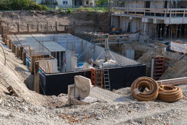 Binanın temelinin atıldığı bir inşaat sahasında çalışmalar sürüyor. Bu şehir projesinde ilerlemeler devam ederken ağır makineler, iskeleler ve işçiler mevcut..