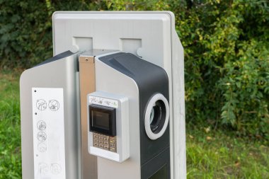 Elektrikli araba pillerini şarj etmek için modern, şık bir sütun yeşil bitkilerle çevrilidir. Kapat..