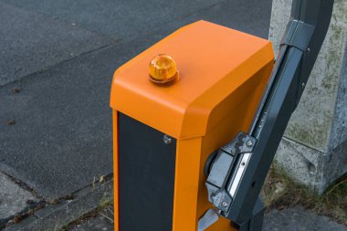Bu bariyer, üzerinde uyarı ışığı bulunan parlak turuncu bir renge sahip, bir şehir caddesinde konumlanmış, kısıtlı erişim ya da inşaat alanını gösteriyor..