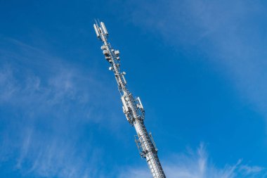Telekomünikasyonu kolaylaştıran sayısız anten ve teçhizatın yer aldığı, parlak mavi gökyüzünün arka planına karşı yüksek bir iletişim kulesi yükseliyor..