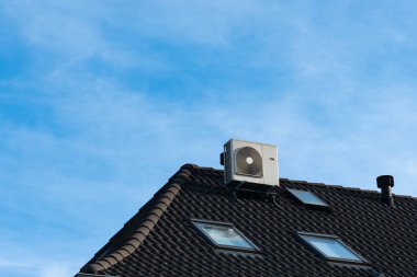 Açık mavi gökyüzü ve dağınık bulutlarla bir binanın çatısına güvenli bir şekilde bir klima yerleştiriliyor..