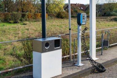 Otomobil yıkama istasyonunda açık bir günde arka planda ağaçlar ve evler bulunan çimenli bir tarlaya yakın bir yerde bulunan hava pompası ve çöp kutusu bulunur..