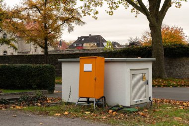 Turuncu kapılı turuncu bir araç kutusu sessiz bir yolun kenarında duruyor. Etrafı yapraklarla ve ağaçlarla çevrili. Parlak sonbahar renkleriyle..