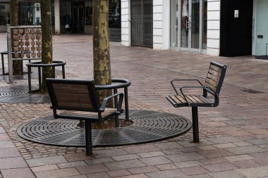 Kalabalık bir kentsel alanda ağaçların etrafına gösterişli banklar yerleştirilir, yoldan geçenleri iyi tasarlanmış bir kaldırımda oturup dinlenmeye davet edilir..