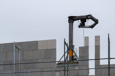 Bir inşaat robotu, gündüz operasyonları sırasında bulutlu bir gökyüzünün altında, iskelelerle çevrili bir inşaat sahasına beton bloklar yerleştirir..