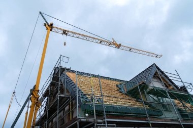İnşaat vinci, çatıda yenilenen malzemeler barındırır. İnşaat iskelesi ve bulutlu gökyüzü yapıda devam eden çalışmaları gösteriyor.