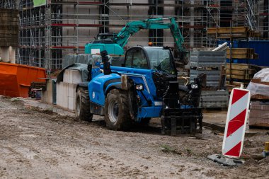 İnşaat alanında mavi bir telsizci var. Binanın etrafı yapı iskelesi, malzeme ve ekipmanlarla çevrili olup, devam eden inşaat faaliyetlerini ön plana çıkarıyor.