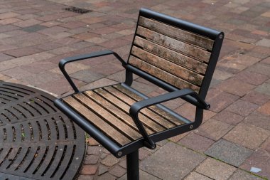 Ahşap bir park bankı şehir merkezinde kaldırım kenarında duruyor, ziyaretçileri gün boyunca çevrede oturmaya ve eğlenmeye davet ediyor..