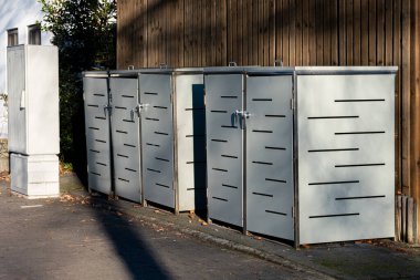 Bir sıra parlak, modern metal depolama birimleri güneşli bir günde ahşap bir çitin karşısında otururlar. Temiz çizgiler ve yapıların minimalist tasarımı çağdaş bir kentsel estetik yaratıyor..