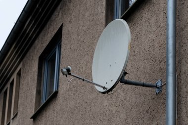 Büyük bir uydu anteni güvenli bir şekilde bir yerleşim yerinin dış duvarına bağlıdır. Yapı kentsel bir ortamda yer alıyor ve bu da televizyonun çekmesinde kullanıldığını gösteriyor..