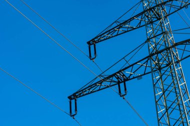 Close-up of a high-voltage transmission tower, electricity pylon, against a clear blue sky. The metal structure of the tower is prominently displayed. clipart