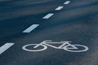 Asfalt bir yolda temiz bir bisiklet yolu izi görülebilir. Bisikletin beyaz çizgisi, sokak çizgileri ve yumuşak gölgelerle çevrili bisikletçiler için belirlenmiş bir alanı gösteriyor..