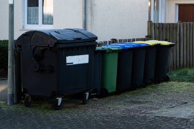 Farklı renkte atık kutuları yerleşim yerlerinin olduğu cadde boyunca düzgünce düzenlenmiştir. Bu kaplar arasında geri dönüşüm ve atık imhası için siyah, yeşil, mavi ve sarı çöp bidonları yer alıyor..