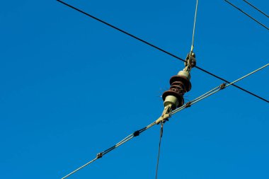 Işıl ışıl mavi gökyüzüne karşı bir konnektör bulunan elektrik hatlarının yakın plan görüntüsü. Metal yapılar, şehirdeki enerji dağılımını destekleyen altyapıyı vurguluyor..