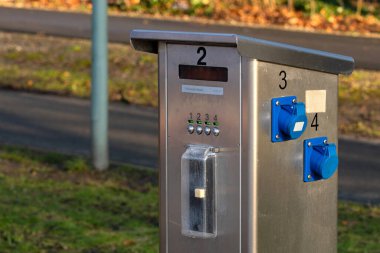 A sleek payment kiosk stands near a walking path in a public park. Visitors can use the interface to pay for park access. The setting features greenery and fallen leaves typical of autumn. clipart