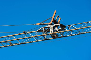 Uzun bir vinç parlak mavi bir gökyüzüne karşı duruyor, metal iskeleti ve kabloları sergiliyor. Bu inşaat makineleri kentsel alanlarda ve sanayide projeler inşa etmek için hayati önem taşıyor..
