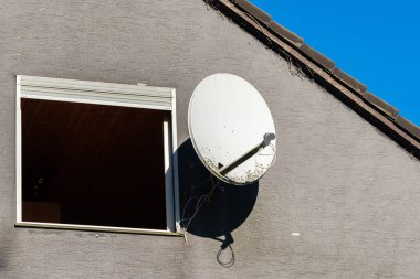 Güneş ışıl ışıl parlayan gri bir binanın penceresine yuvarlak bir uydu anteni monte edilir. Kurulum, modern teknolojiyi kentsel bir ortamda yansıtıyor ve iletişimi geliştiriyor..