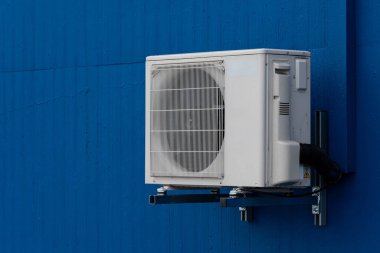 Mavi bir duvara işlevsel tasarımını gösteren beyaz bir klima monte edilir. Bu birim, modern bir açık hava ortamında etkili bir soğutma için konumlandırılmıştır..