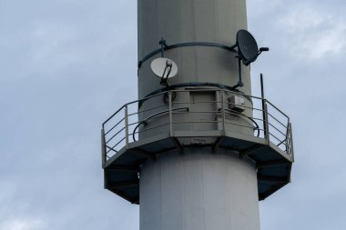 Yüksek bir iletişim kulesi bulutlu bir gökyüzüne yükseliyor, korkuluklara uydu anteni monte ediliyor. Yapı sinyal göndermek için sağlam ve gerekli görünüyor..