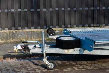 Yanında tek bir tekerlek bulunan asfaltlı bir yüzeye yerleştirilmiş bir karavan. Arkaplanda, aydınlık gün ışığında karanlık ve dikey bir çit sergileniyor..