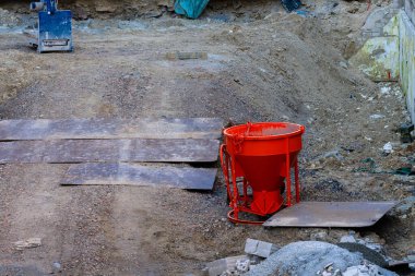 Bir inşaat sahasında yerde, çakıl ve toprakla çevrili parlak turuncu bir mikser bulunur. Metal levhalar, inşaatçılar için çalışma alanı oluşturarak yerde yatıyordu..