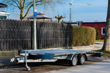 Metalik bir römork, arka planda inşaat vinçleri olan bir çitin yanına park edilmiş. Güneş parlıyor ve bölge sessiz görünüyor. Bu da geçici bir durak olduğunu gösteriyor..