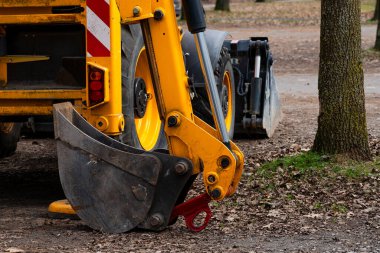 Sarı inşaat kazıcısı parktaki peyzaj işleri için hazırlanıyor. Yere yerleştirilmiş bir kürek ile... Düşen yapraklar ve kir arasında....