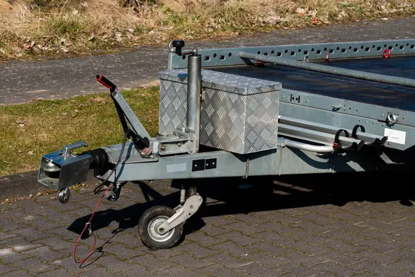 Asfaltlı bir yüzeye uzanan eklentilerle birlikte bir römorkun yakın görüntüsü. Güneş metalik kısımları aydınlatıyor, yapılarını ve işlevselliklerini vurguluyor..