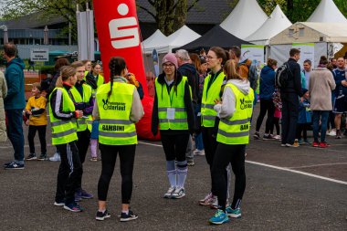 ALMANY, PADERBORN, 77 EASTER RUN - 04-19-2025. Parlak sarı yelekli bir grup gönüllü bir topluluk etkinliğine hazırlanırken sohbete dalıyorlar. Sadece editör kullanımı.
