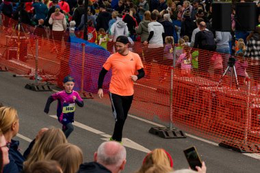ALMANY, PADERBORN, 77 EASTER RUN, 04-19-2025. Pembe tişört giyen genç bir koşucu bir yetişkine ayak uydurup ilham verici bir takım çalışması ortamı yaratıyor. Sadece editör kullanımı.