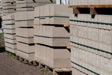 Sağlam beton bloklar bir inşaat alanındaki ahşap paletlerin üzerine düzgünce istiflenir. Parlak güneş ışığı, çeşitli inşaat projelerine hazır olduklarını belirterek, onların dokusunu vurguluyor..