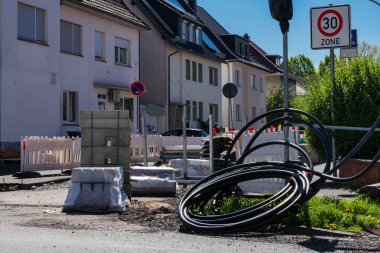 İnşaat malzemeleri yığıldı ve bir şehir caddesinde elektrik kabloları sarıldı. Yerleşim yerleri açık mavi gökyüzünün altında cadde boyunca uzanır..