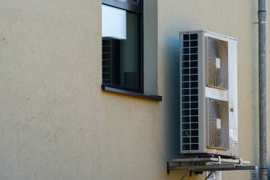 Büyük bir havalandırma ünitesi binanın yan tarafına güvenli bir şekilde yerleştirilmiş ve yakınlardaki pencereden temiz mavi bir gökyüzü görülebiliyor. Birim, iç mekanın soğutulmasına katkıda bulunur..