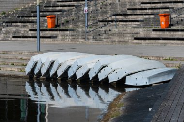 Çok sayıda kayık sakin bir su yüzeyi boyunca sakin bir yerde beton basamakların yanında dizildi. Sahne bir durgunluk anı yakalar, ince yansımalarla görünür..