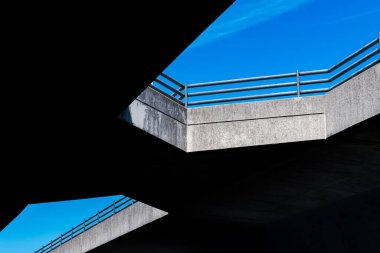 Mavi gökyüzüne karşı mimari köprü şekillerinin soyut görüntüsü. Işık ve gölgenin etkileşimi somut tasarımın detaylarını vurgular. Bir şehir güzelliği görüntüsü.