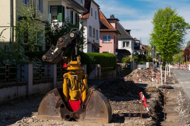 Tamirat yapılan bir yerleşim yerinin üzerinde ağır inşaat makineleri duruyor. İşçiler bölgeyi gelişmelere hazırlarken parlak güneş manzarayı aydınlatıyor..