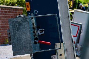 Metal kontrol paneli, kolları ve düğmeleri olan bir inşaat alanında duruyor. Çevredeki yeşillik ve ekipman gündüz saatlerinde aktif bir çalışma olduğunu gösteriyor.