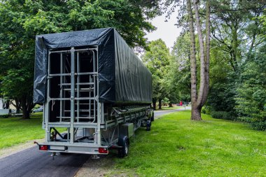 Muşamba kaplı bir römork, yemyeşil ağaçlarla çevrili dolambaçlı bir patika boyunca park edilmiştir. Sahne, gündüz vakti doğa dolu bir ortamda huzurlu bir anı yakalıyor..