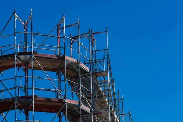 İskele yapısı belirgin bir şekilde parlak mavi bir gökyüzünün altında sergilenmektedir. Metal çerçeve inşaat çalışmalarını destekliyor, inşaat çalışmalarının ilerlemesini gösteriyor.